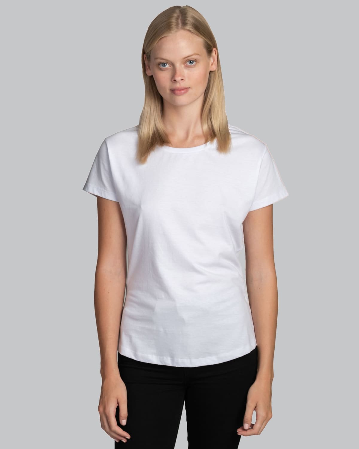 Woman in a plain white T-shirt and black pants standing against a gray background.