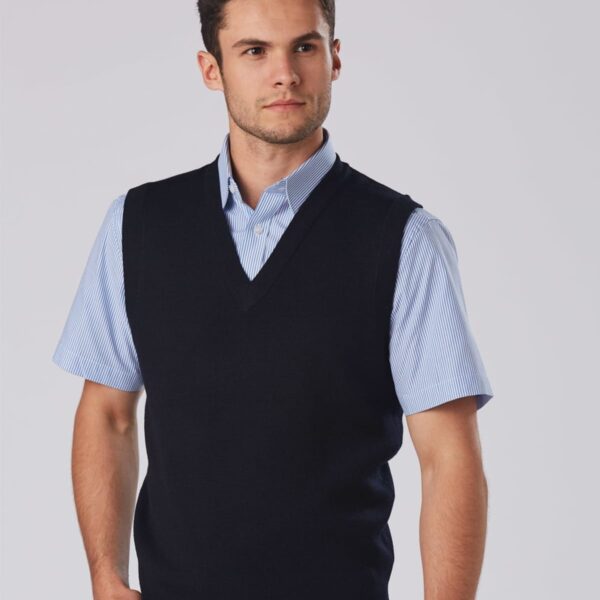 A person wearing a light blue short-sleeve shirt with a navy blue V-neck sweater vest stands against a plain background. They have short dark hair and a neutral expression.