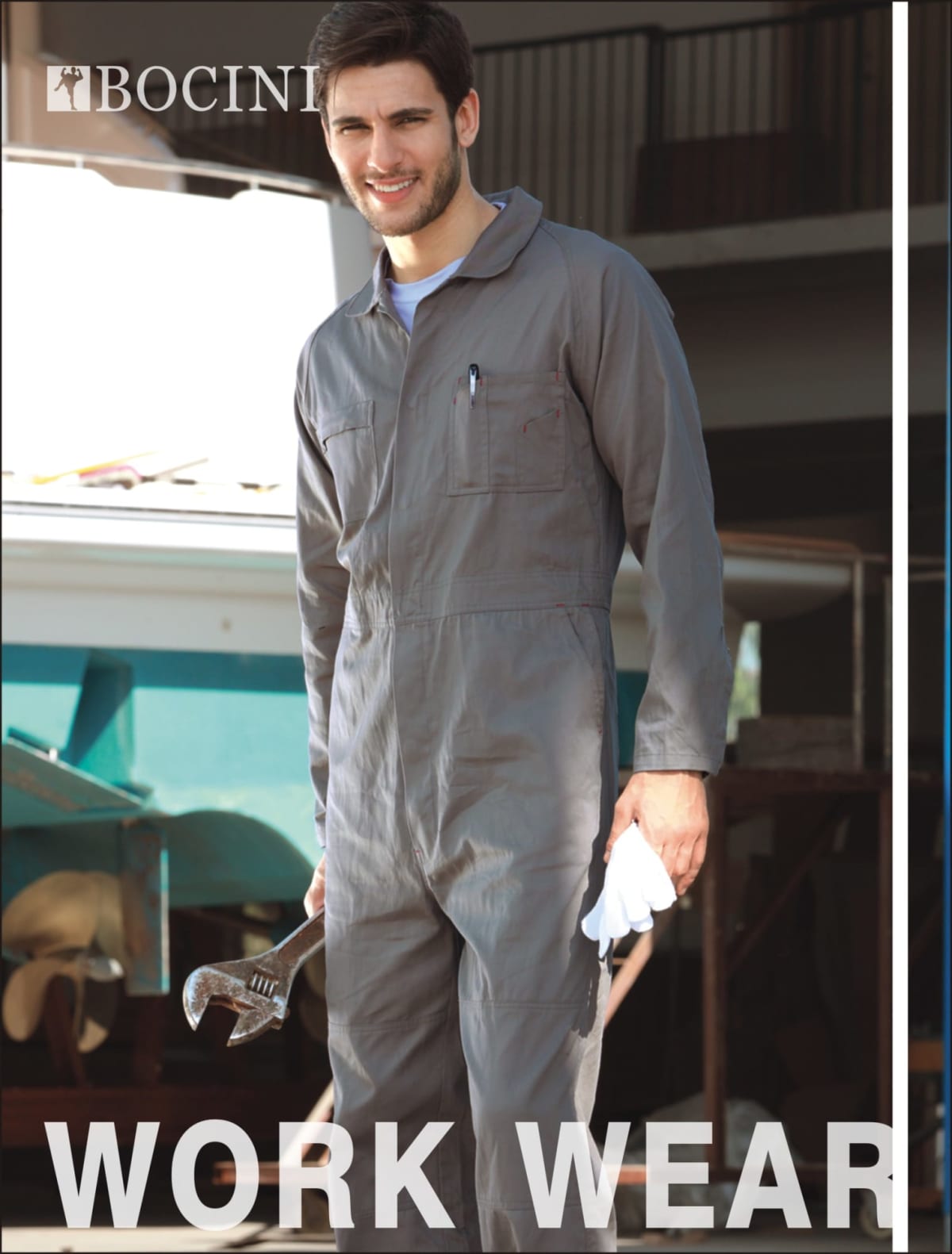 A man in a gray coverall stands holding a large wrench and a white glove. He is smiling and outdoors. The word BOCINI is in the top left corner, and WORK WEAR is written at the bottom in bold letters.
