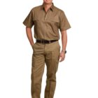 A man wearing a short-sleeved khaki uniform with front pockets, black belt, and black shoes stands smiling with one hand in his pocket against a plain white background. He is wearing a watch on his left wrist.