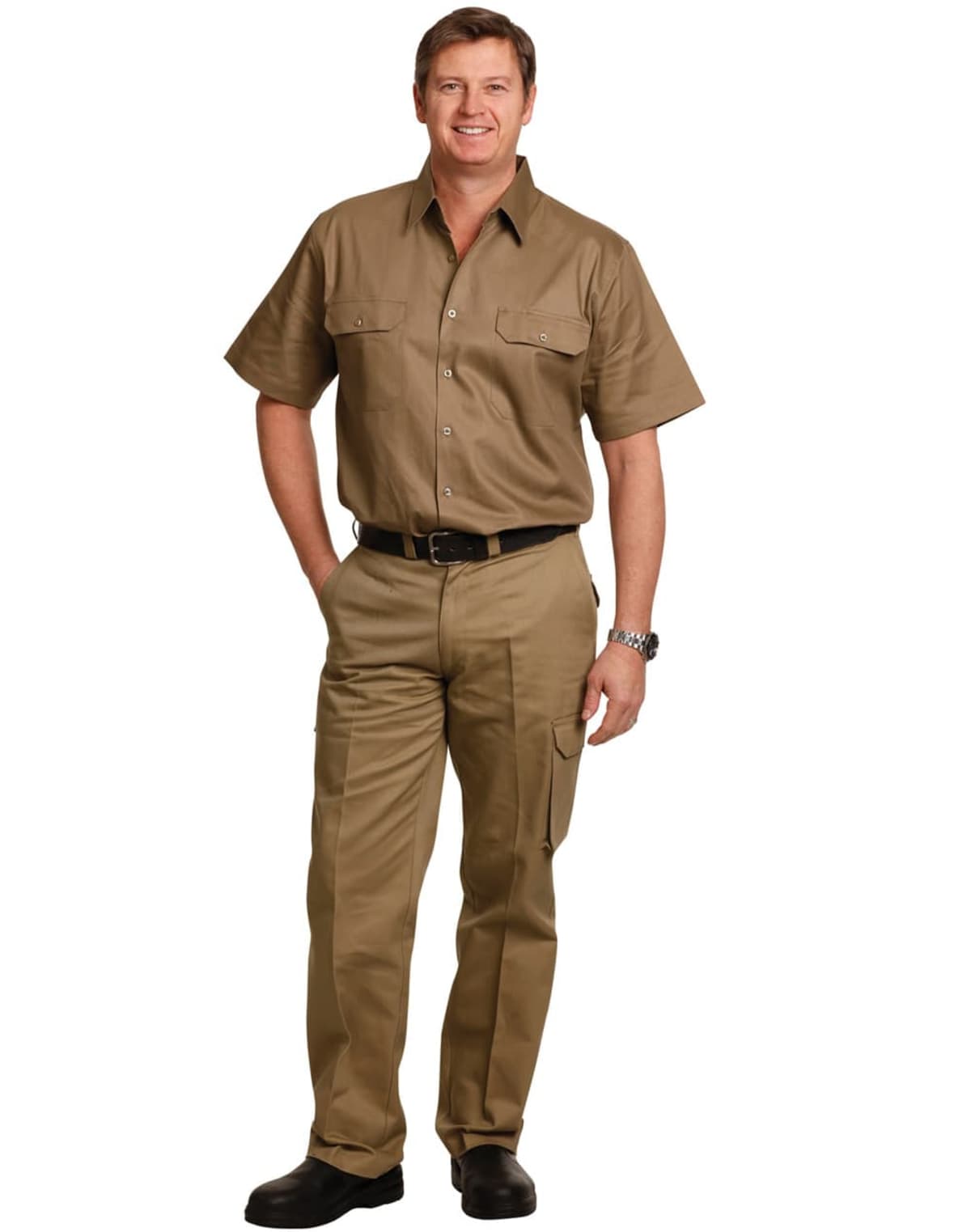 A man wearing a short-sleeved khaki uniform with front pockets, black belt, and black shoes stands smiling with one hand in his pocket against a plain white background. He is wearing a watch on his left wrist.