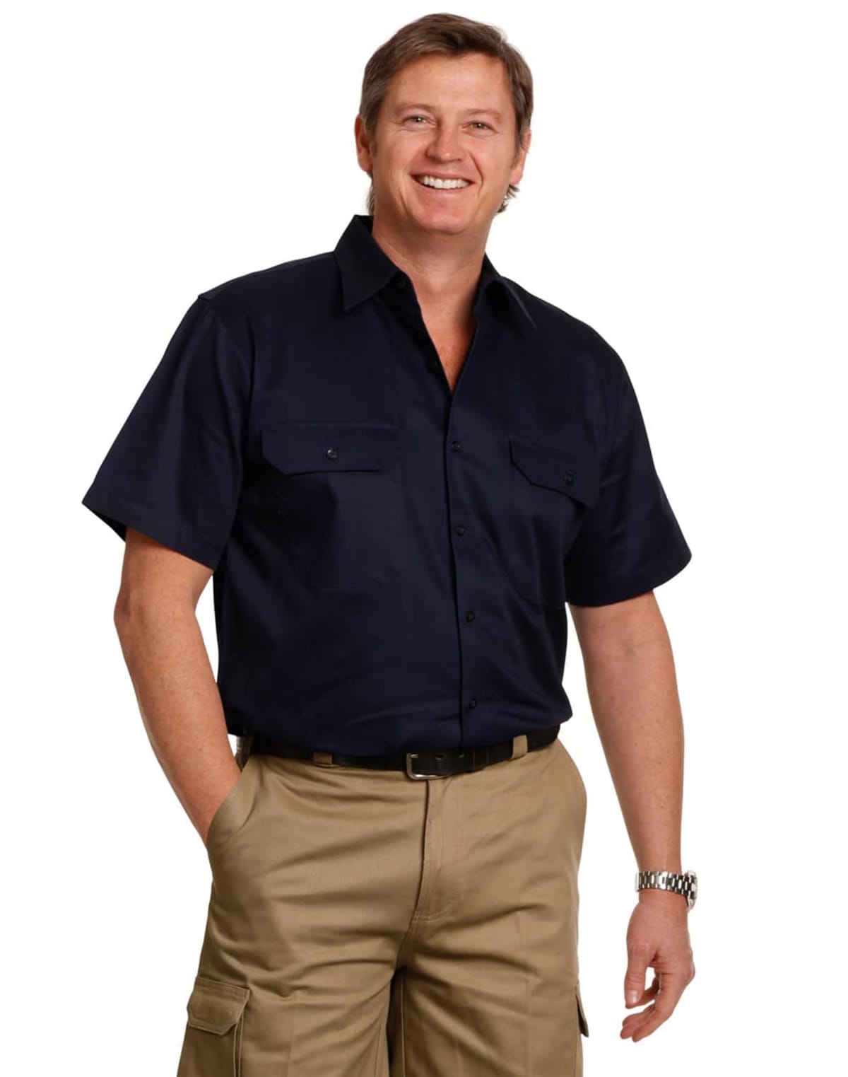 A man smiling, wearing a navy short-sleeve shirt and khaki pants with cargo pockets. He stands with one hand in his pocket against a white background.