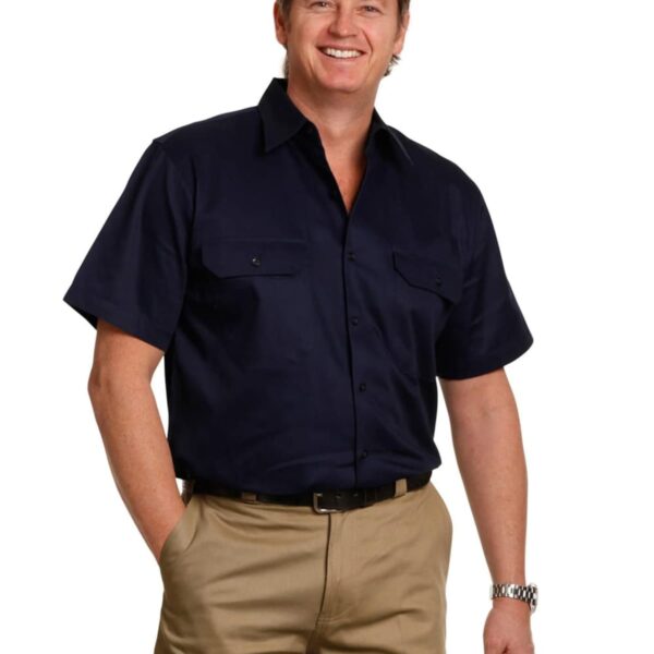 A person in a short-sleeve navy shirt and khaki pants smiles while standing. They have a relaxed posture, with one hand in their pocket. The background is plain white.
