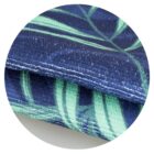 Close-up of a fabric with a leafy pattern. The pattern features green leaves on a dark blue background, and the fabric has a textured, woven appearance. The image is circular, focusing on the fabrics detail.