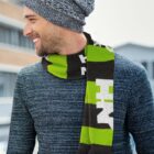 Smiling man in a gray knit sweater and matching beanie, with a green, black, and white scarf, standing outdoors with blurred buildings in the background.