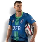 A man in a blue and green rugby jersey holds a rugby ball under his left arm. He gazes to his right, standing against a white background. Logos on the jersey include BFB and other rugby-related designs.