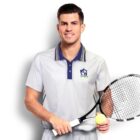 A person in a white tennis polo shirt holding a tennis racket and ball stands smiling against a white background. Their hair is short and styled neatly.