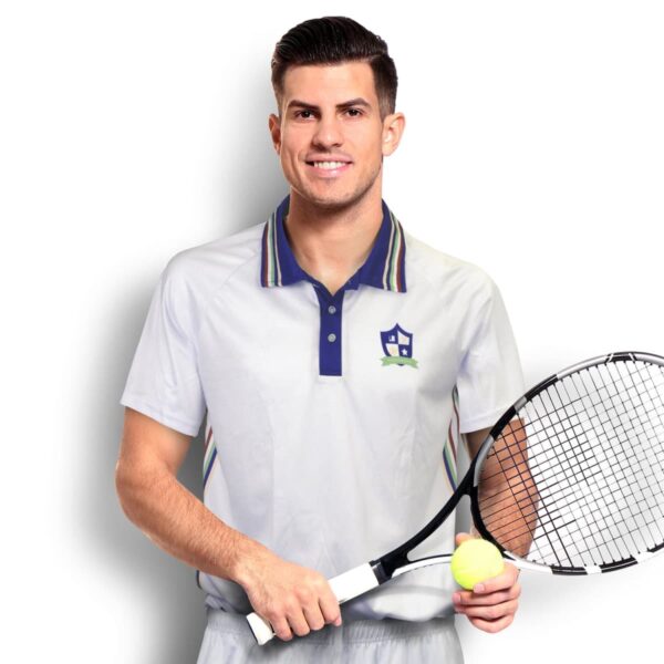 A man in a white tennis outfit holding a racket and a tennis ball stands against a white background. He is smiling and has short, dark hair.