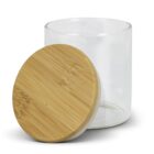 A transparent glass jar with a flat base is opened, and its round wooden lid with visible grain patterns rests beside it. The jar and lid are positioned against a white background, highlighting their simple, elegant design.