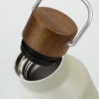 A wooden cap with a metal handle beside the open mouth of a white bottle.
