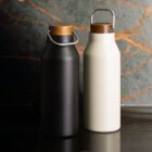 Black and white metal water bottles with wooden lids on a dark surface.