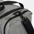 Close-up of a gray fabric bag with a black zipper and an attached black shoulder strap.