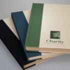Three hardcover books, one labeled Charity Foundation, stacked on a light surface.