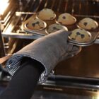 A hand wearing an oven mitt takes a tray of baked muffins from an oven.