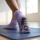 Person wearing fuzzy purple socks standing on a blue yoga mat in a bright room.