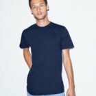 A person with short hair is wearing a navy blue T-shirt and light blue jeans, standing against a plain white background. They have one hand in their pocket and a relaxed expression.