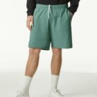 Person wearing green shorts, white sneakers, socks, and a black sweatshirt against white background.