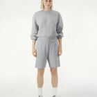 Person wearing a gray sweatshirt and gray shorts, standing against a plain white background.