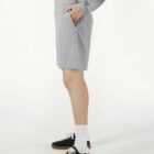 Person wearing gray shorts, a gray sweatshirt, white socks, and black sneakers, side view.