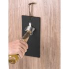 Hand opening a bottle with a wall-mounted metal bottle opener on a wooden surface.