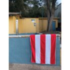 A red and white striped towel hangs on a tiled wall near a shower and a yellow building.
