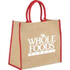 A jute tote bag with red handles and Whole Foods Market logo in white.