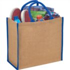 A jute tote bag with blue handles filled with various travel items.