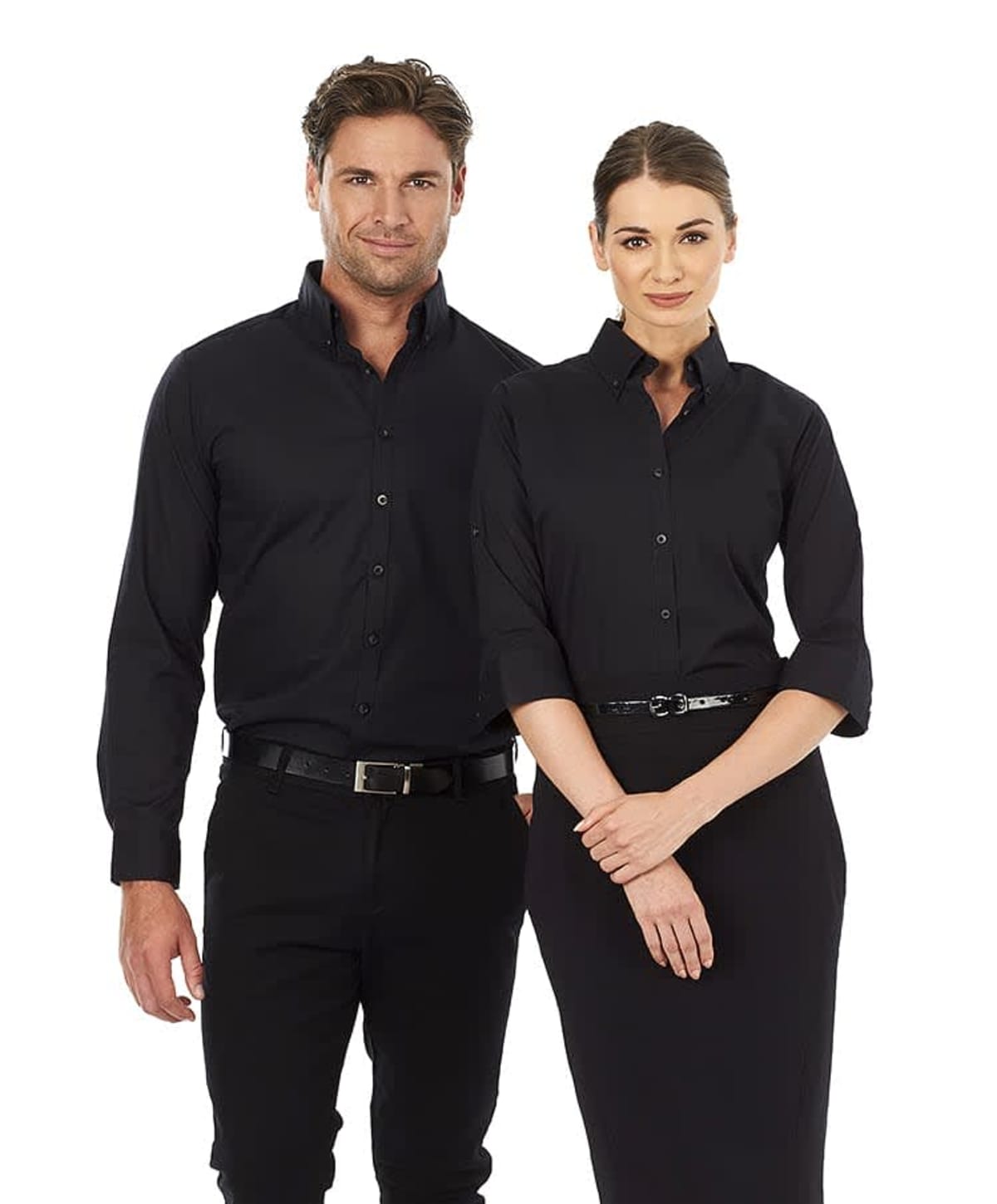 A man and a woman are standing together, both wearing black button-up shirts. The man has his hands by his sides, and the woman is smiling with her hands clasped in front. Both are dressed in a professional manner.