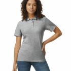 Woman in a grey polo shirt and blue jeans standing with one hand on her hip, smiling.