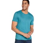 Man wearing a teal T-shirt and dark jeans, standing against a white background. He is smiling and looking to the side, with his hands clasped in front of him.