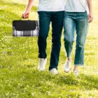Couple walking on grass, carrying a black and white checkered bag.
