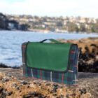 Plaid picnic blanket folded on a rocky shoreline with water and a town in the background.