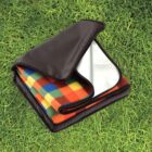 Folded multicolored picnic blanket with foil underside on grass.