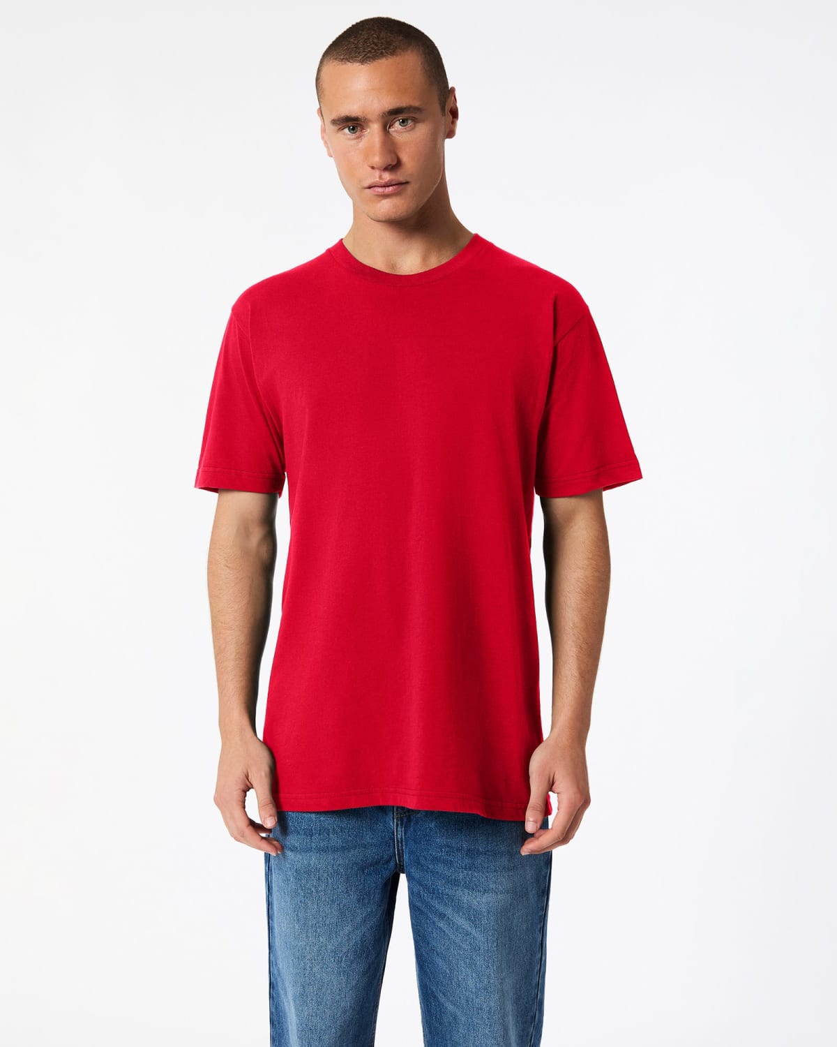 A person wearing a plain red T-shirt and blue jeans stands facing forward against a white background.