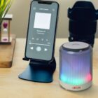 Smartphone on stand playing a podcast next to a colorful LED Bluetooth speaker.