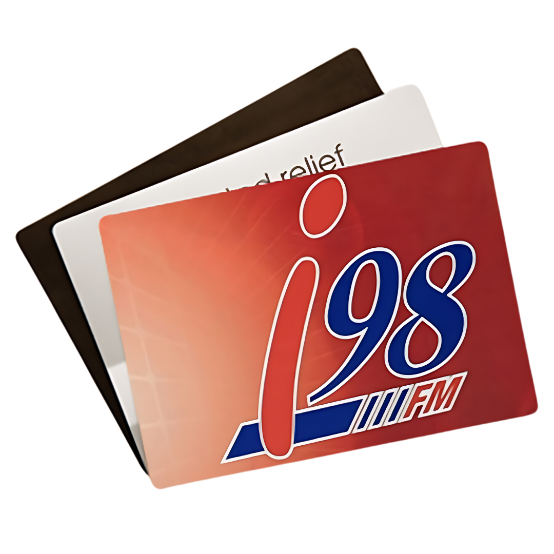 Displayed on a Deluxe Promotional Counter Mat (42x29x0.3cm), three overlapping cards showcase a striking design: the front card is red with i98 FM in bold, the middle card is white with partial relief text, and the back card is solid black.