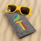 Yellow sunglasses and a gray box with a colorful logo and FALCON WILSON SERVICES text, resting on sand.