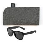Black sunglasses with a classic frame and dark lenses are displayed in front of a gray textured case with a small black label.