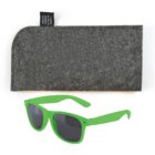 Green sunglasses with dark lenses sit in front of a gray, textured case made from recycled plastic bottles. The case has a small black tag.