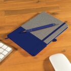 A blue and gray notebook lies on a wooden desk with a matching blue pen placed on top. Part of a white keyboard and a white computer mouse are visible on the desk.
