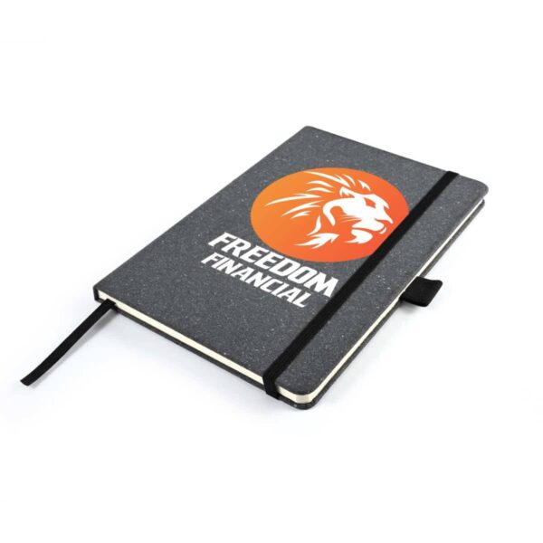 A grey notebook with a black elastic band and pen holder, featuring the Freedom Financial logo: a white lions profile inside an orange circle. The notebook is closed and placed on a white background.