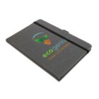 A gray notebook with the ecogenius logo and the phrase THINK SUSTAINABLY! The logo features a carrot with green leaves above the text. The notebook is secured with a black elastic band.