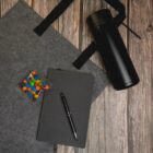 Notebook, pen, candy, thermos, and bag on a wooden surface.