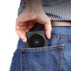 Hand placing a small black wireless charger into a back pocket of blue jeans.