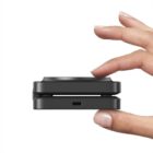Fingers holding a compact black camera with a USB-C port.