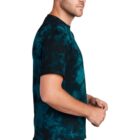 Man in blue tie-dye shirt and jeans stands sideways, looking forward.