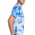 Man in blue tie-dye shirt and jeans, standing sideways against a white background.