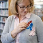 Woman attaching Label Pins—red, blue, and pink—to her cardigan in a library.