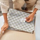 A person wearing a sweater and beige pants is opening a cardboard box. Inside, theres patterned wrapping paper and a small, round label with the text Style Form visible. The scene is set against a neutral backdrop.
