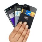A hand holding three smartphones with cardholders attached to the back. Each phone has a card partially visible, showcasing different designs and colors. The nails are painted beige. The phones and cards are arranged in a fan-like shape.
